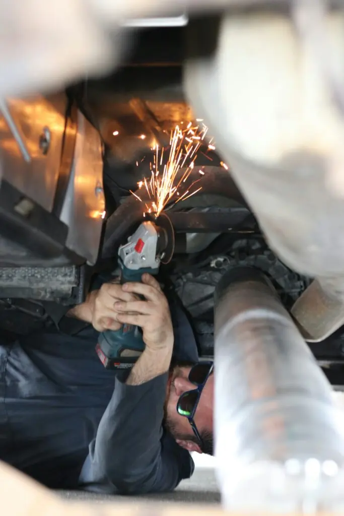 Symbolbild: Mechaniker arbeitet mit einem Winkelschleifer am Unterboden eines Autos, Funken sprühen